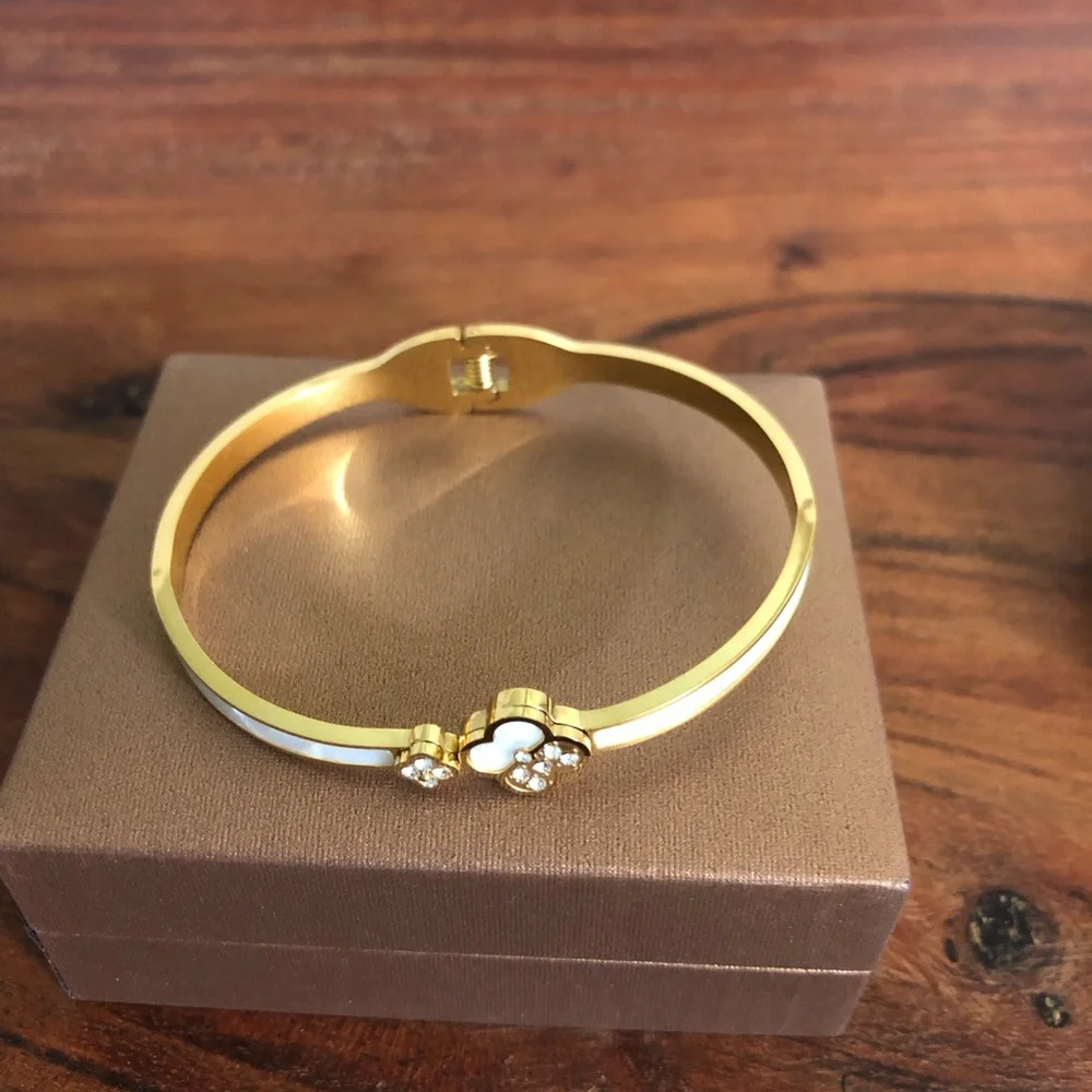 gold-toned hinged bangle bracelet featuring white clover motifs and crystal New